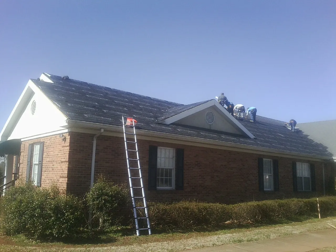 Crew tearing shingles off a brick ranch roof with a ladder set — Emergency Roof Repair work by our crew in Hornbrook