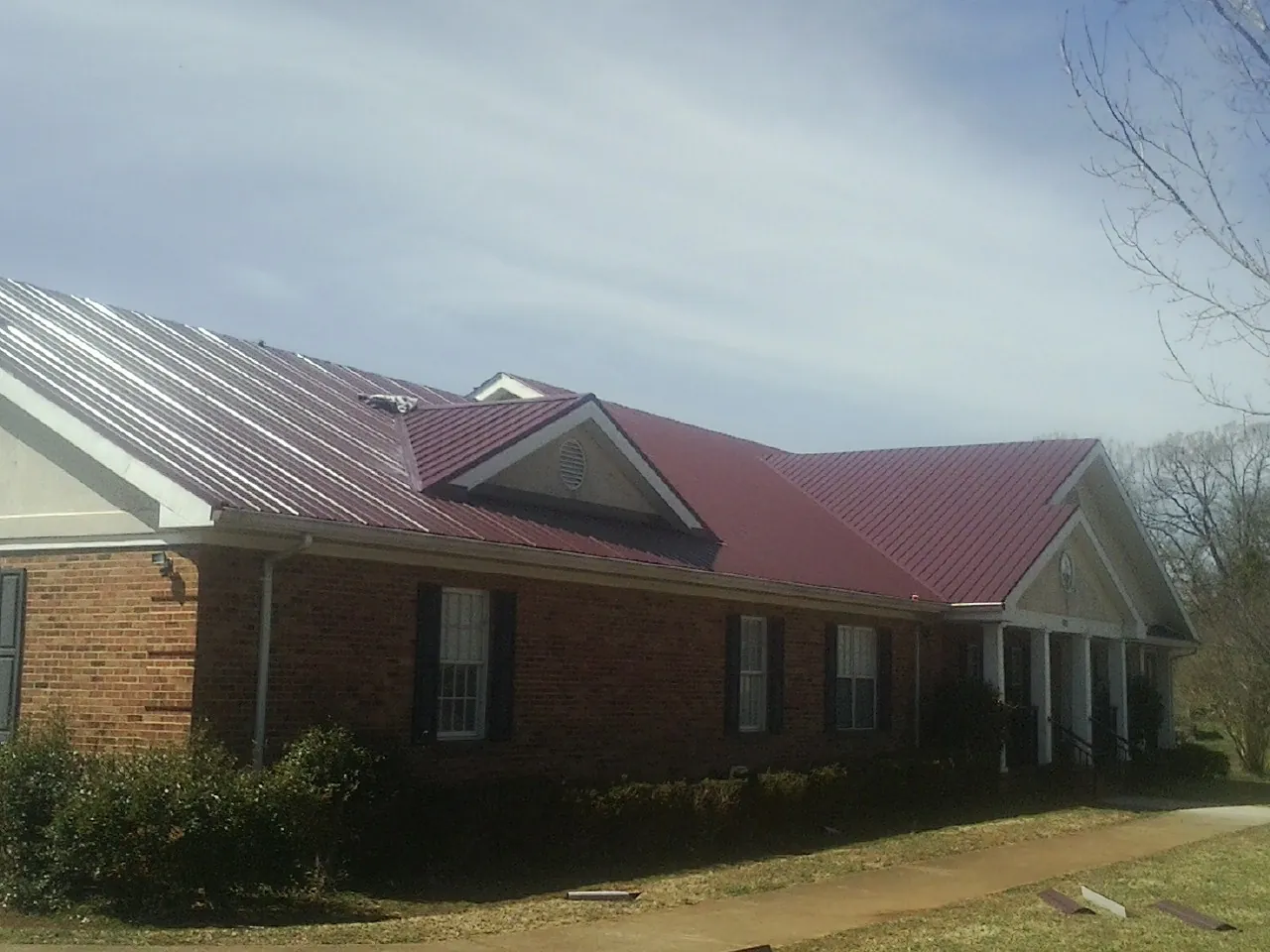 Red metal roof with gabled entries on a long brick building, from a Hail Damage Roof Repair job in Hornbrook